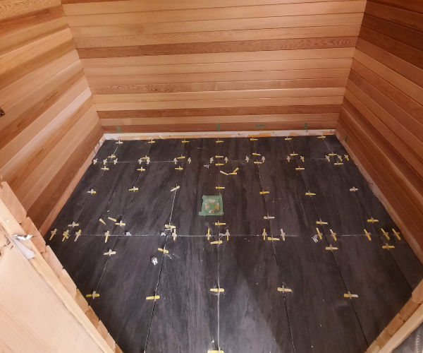 Precision floor tile leveling installation inside custom cedar sauna build.